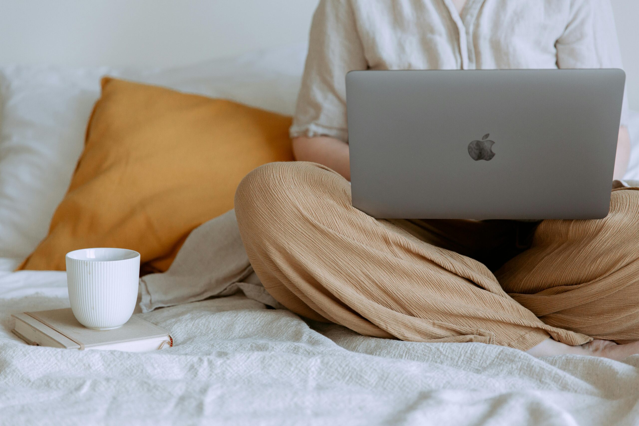 A person sits in bed working on their laptop with a coffee next to them.